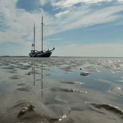 Die Minerva trockengefallen im Watt mit Spiegelung im Wasser